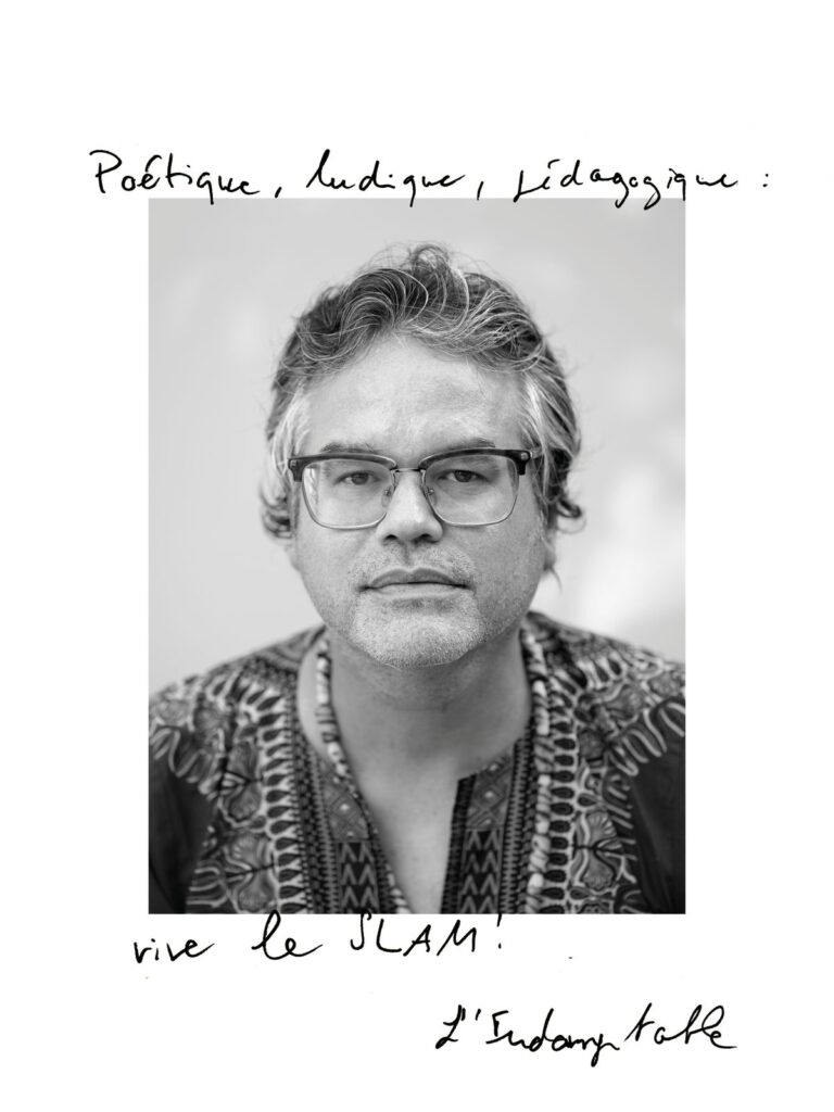 صورة شخصية لـ L’Indomptable بعدسة جورجيا. الجملة المكتوبة باليد: «Poétique, ludique, pédagogique : vive le slam !»